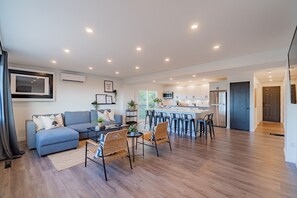 Una sala de estar moderna con sofá, mesa de centro y sillas, una cocina con taburetes de bar y un comedor con mesa y sillas.