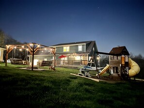 Enjoy a backyard retreat with a swing set, playhouse, and slide, surrounded by a lawn and a porch with a shaded area.