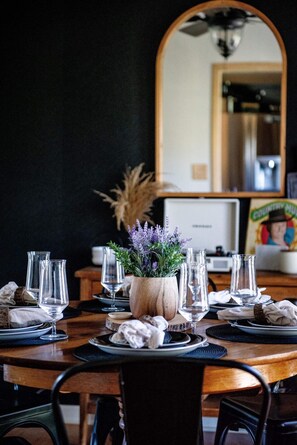 A dining area with a round table set for a meal, featuring glassware and a centerpiece with dried plants.