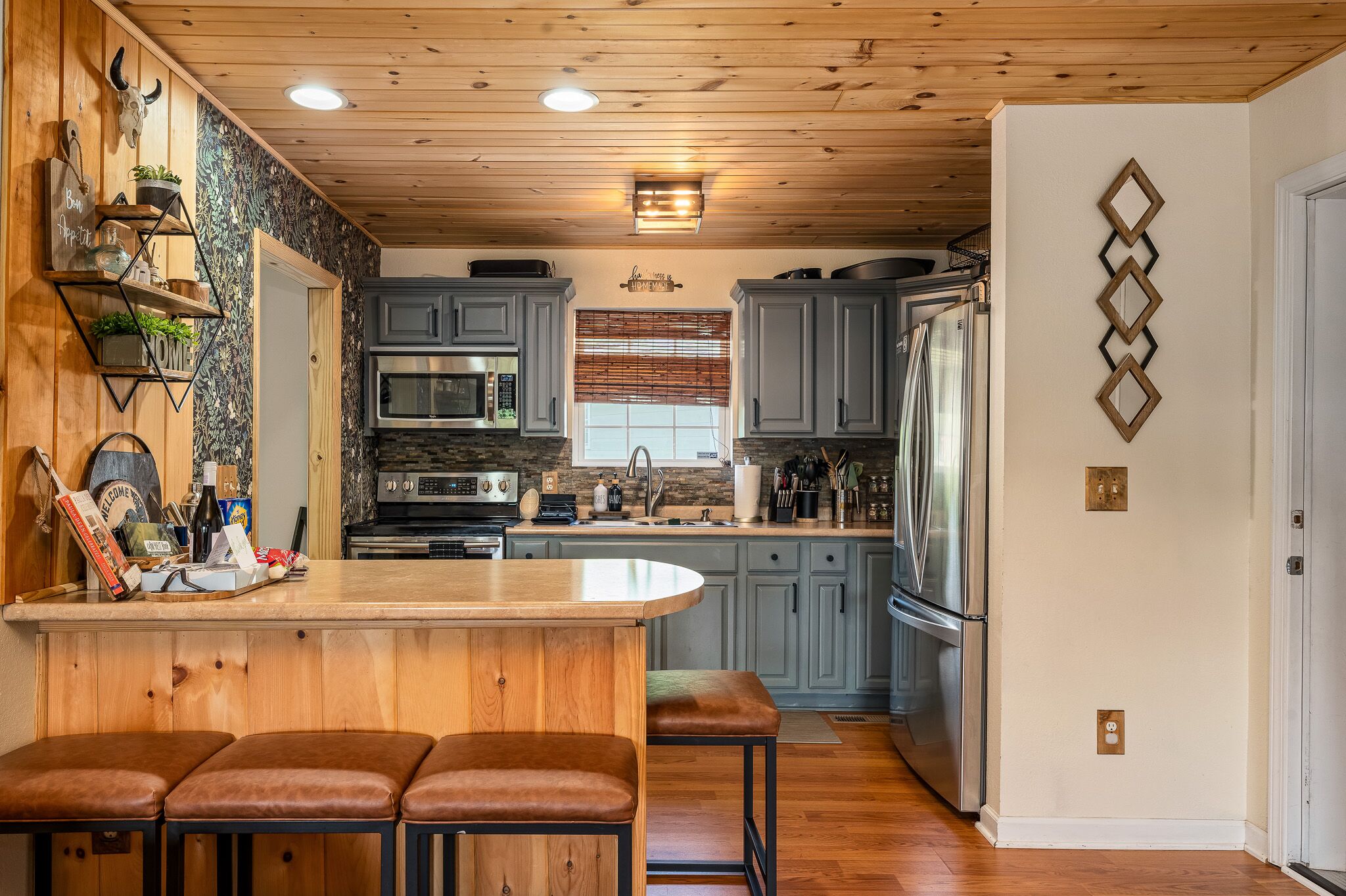 A kitchen with wooden cabinets, a central island with stools, a microwave, and a refrigerator.