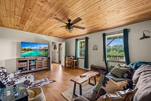 Relax in this spacious living area with a high ceiling, featuring a comfortable sofa, wooden coffee table, and large windows offering views of the surrounding greenery.