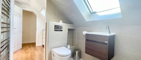 A modern bathroom with a skylight, a toilet, a sink, and a trash can.