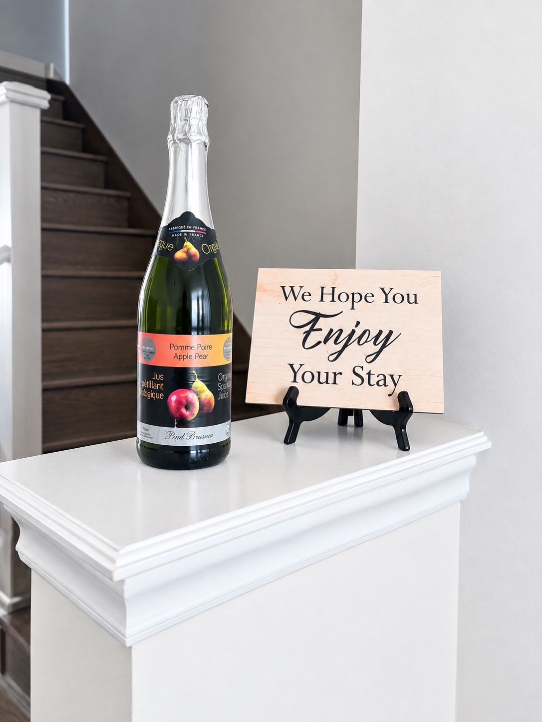 A bottle of wine and a sign on a white mantelpiece.