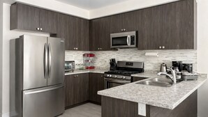 Una cocina moderna con armarios de madera oscura, electrodomésticos de acero inoxidable, encimera de granito y un microondas sobre la estufa.