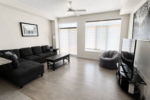 Un salon moderne avec un canapé d’angle, une table basse, un fauteuil poire et un téléviseur à écran plat.