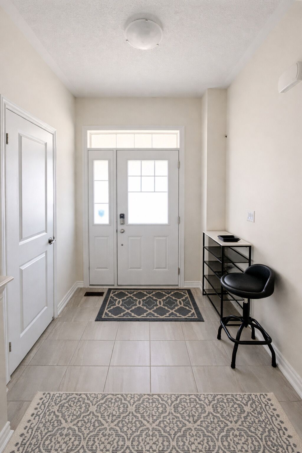 Un couloir avec une porte blanche, une chaise noire et un tapis à motifs.
