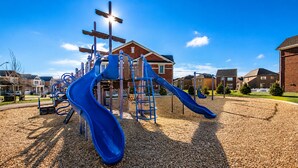 Un parque infantil con toboganes y estructuras para escalar, rodeado de edificios residenciales.