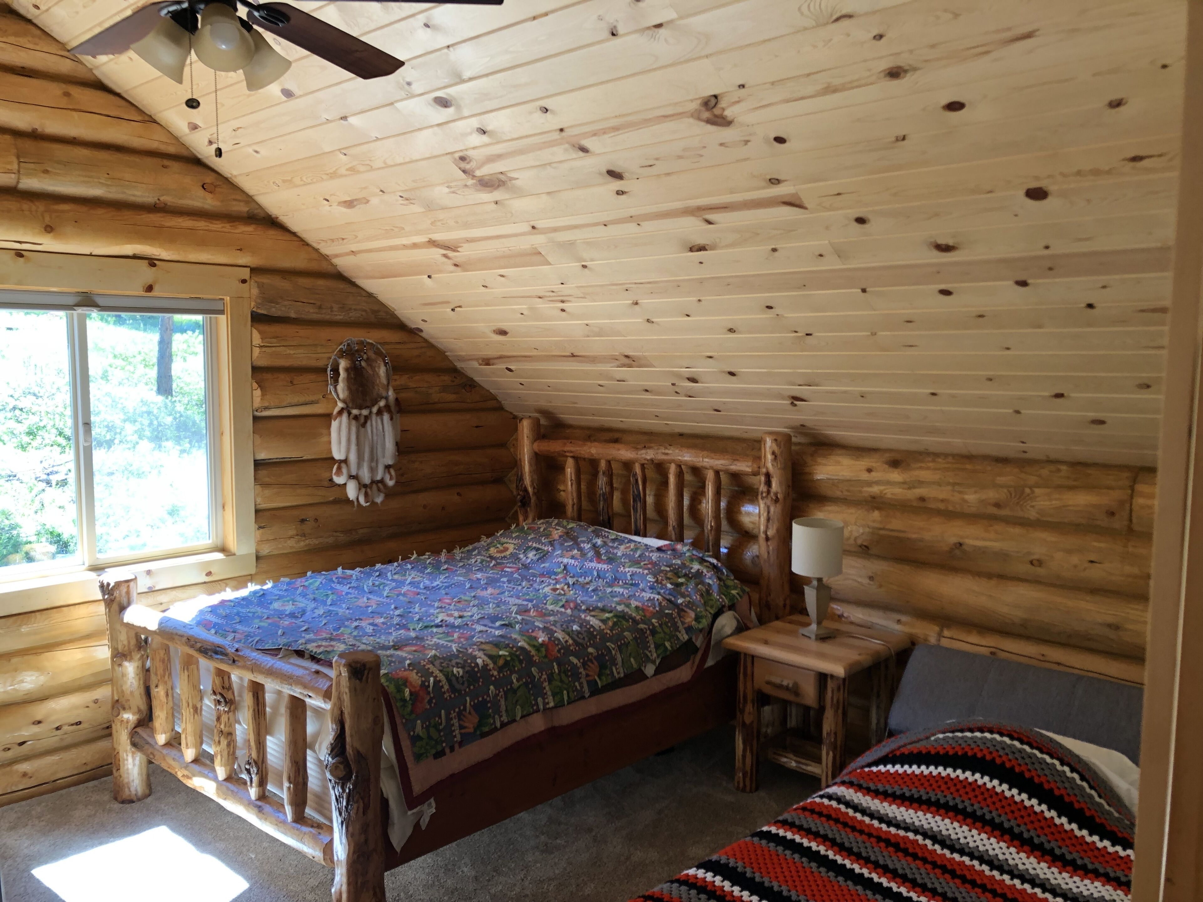 A wooden cabin bedroom with a bed, bedside table, and a window.