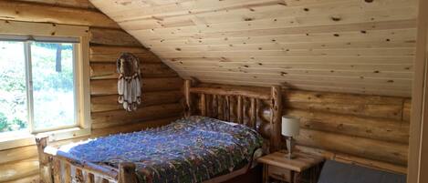 A wooden cabin bedroom with a bed, bedside table, and a window.