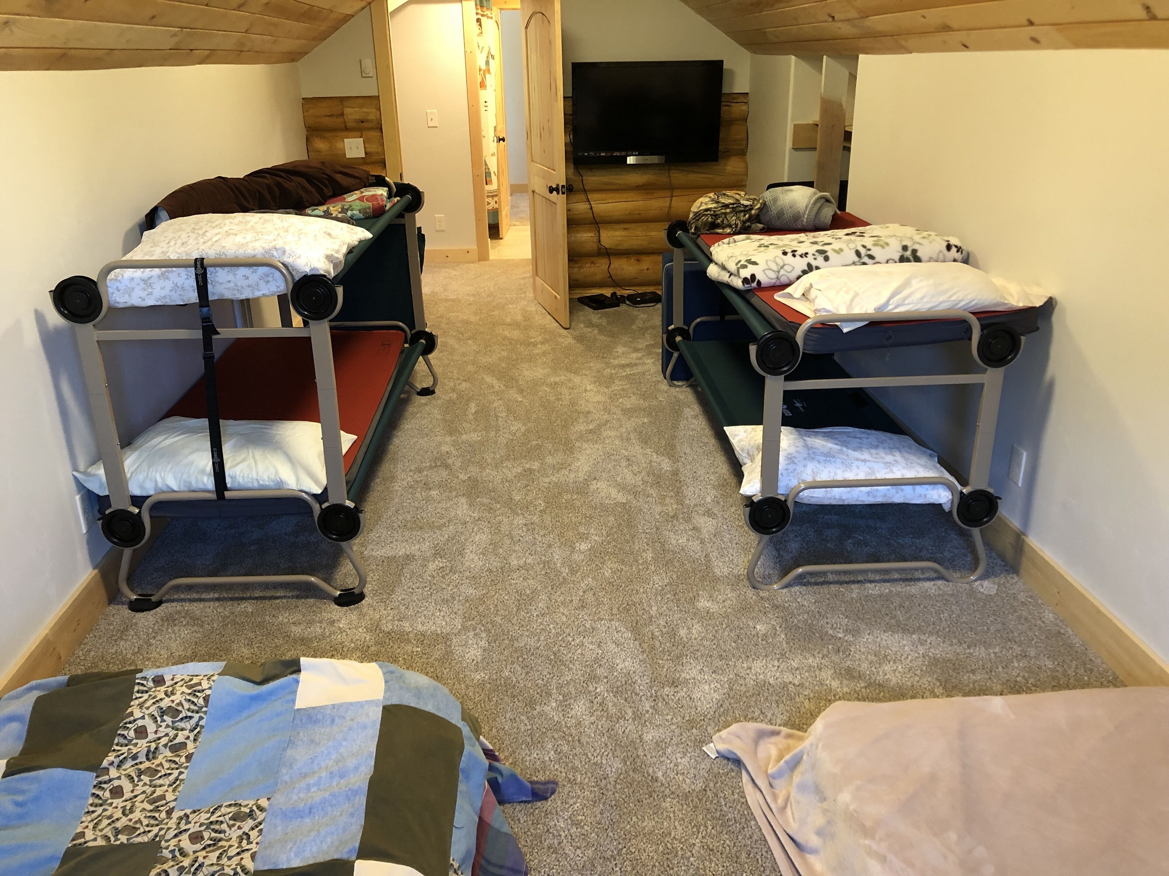 Ett rum med två våningssängar, en tv på väggen och ett heltäckningsmatta på golvet.