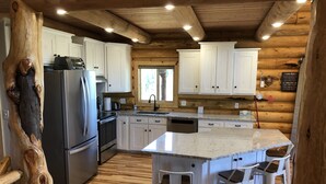 A modern kitchen with white cabinets, stainless steel appliances, and a central island with bar stools. - Private Log Cabin with breathtaking views on 15 acres adjacent to forest service (Council)