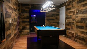 A pool table in a room with wooden panel walls and a neon sign reading "ARCADE".