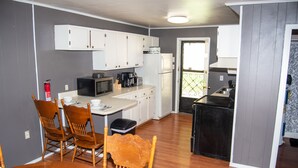 A compact kitchen with white cabinets, a microwave, a refrigerator, and a dining area with wooden chairs and a table set for two.
