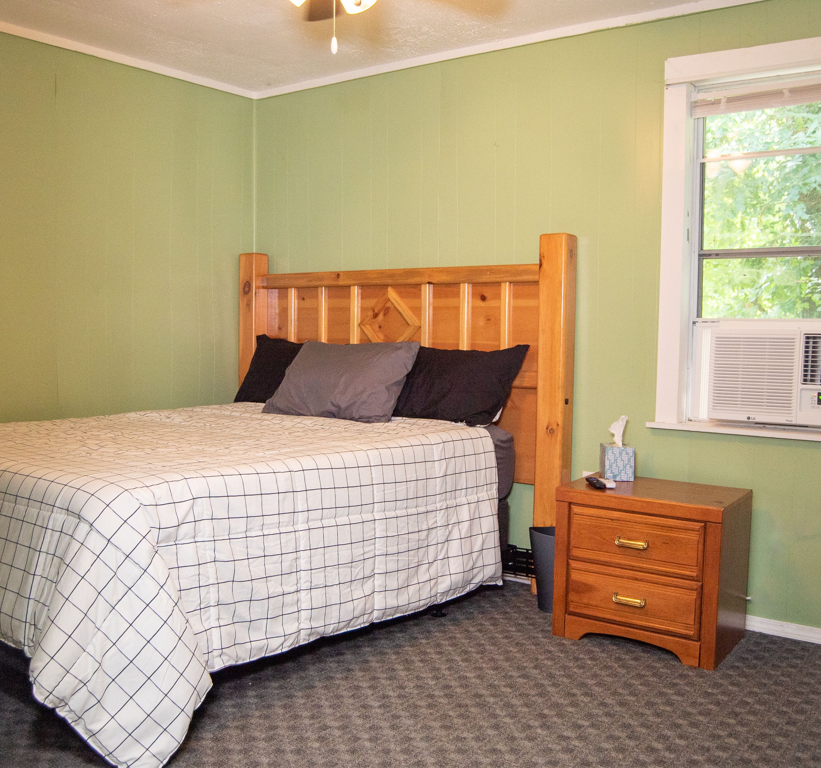 A bedroom with a wooden bed, a nightstand, and a window with an air conditioner.