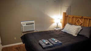 A bedroom with a bed, a bedside lamp, an air conditioner, and a folded towel on the bed.