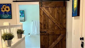 Ein Flur mit einer hölzernen Tür im Bauernhausstil, weißen Wänden und einem weißen Geländer mit Blumentöpfen.