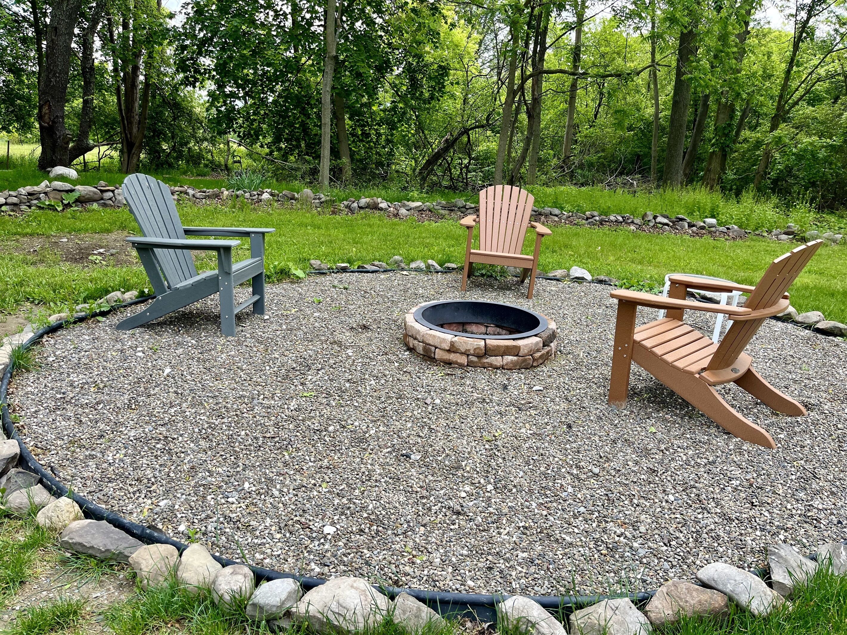A circular gravel area with a fire pit and three Adirondack chairs.