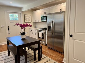 A modern kitchen with white cabinets, stainless steel appliances, and a wooden dining table with a vase of flowers. - Renovated 5 Bedrm/3bath + Swim Spa & Huge Outdoor Space (Goshen)