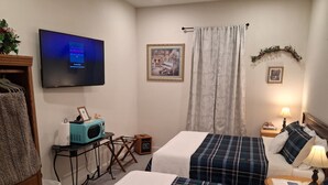 Une chambre d’hôtel avec deux lits, une télévision, une petite table avec un four à micro-ondes, une table de chevet avec une lampe et un tableau accroché au mur.