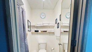 Une salle de bain avec deux toilettes, un rideau de douche, un tapis et des étagères avec des serviettes.