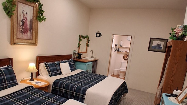 Une chambre d’hôtel avec deux lits, un ventilateur de plafond, une petite table avec une lampe, un miroir et une horloge au mur.