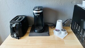 Une petite cuisine équipée d’un grille-pain, d’une machine à café et de deux tasses posées sur une table en bois.