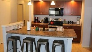 A kitchen with wooden cabinets, a microwave, a stove, and a sink. There are four stools at the island. - Athens city townhouse, 3 bedrooms, 2.5 baths, FREE Wi-Fi, FREE Parking, Deck, 18 (Athens)