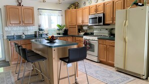 A kitchen with wooden cabinets, a stainless steel microwave, a white refrigerator, and a small island with two bar stools.
