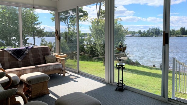 A sunroom with a large window overlooking a lake, furnished with a sofa, chairs, and a small table.