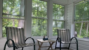 A room with two striped chairs and a small table, large windows with a view of trees, and a white wall.