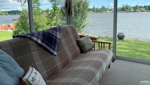 A cozy living room with a plaid sofa, a small table, and a view of a lake with trees and a distant shoreline.