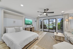 Une chambre d’hôtel moderne dotée d’un grand lit, d’une télévision à écran plat, d’un ventilateur de plafond et d’un balcon offrant une vue sur la ville.