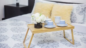 Una bandeja ordenada con un florero de flores blancas, una tetera y dos tazas sobre una cama con colcha estampada.