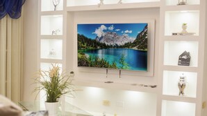 Una sala de estar con un televisor de pantalla montado que muestra un lago de montaña, una mesa de centro de vidrio, una planta en maceta y un sofá azul.