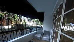 Un balcón con toldo negro, una mesita con una planta y una silla.