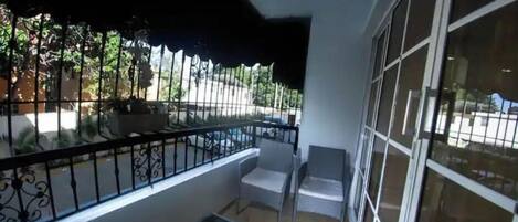 Un balcón con toldo negro, una mesita con una planta y una silla.
