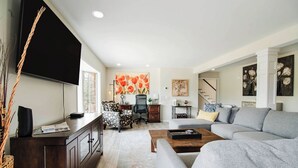 A modern living room with a grey sofa, a wooden coffee table, a dark wooden cabinet, a black TV, and a patterned armchair. - Castle Farms wedding weekend, 7BR (Charlevoix)
