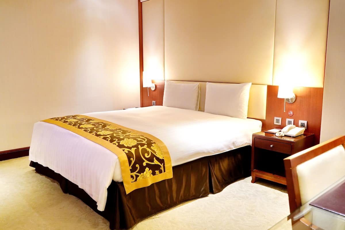 A hotel room with a large bed, bedside lamps, a nightstand with a phone, and a chair.