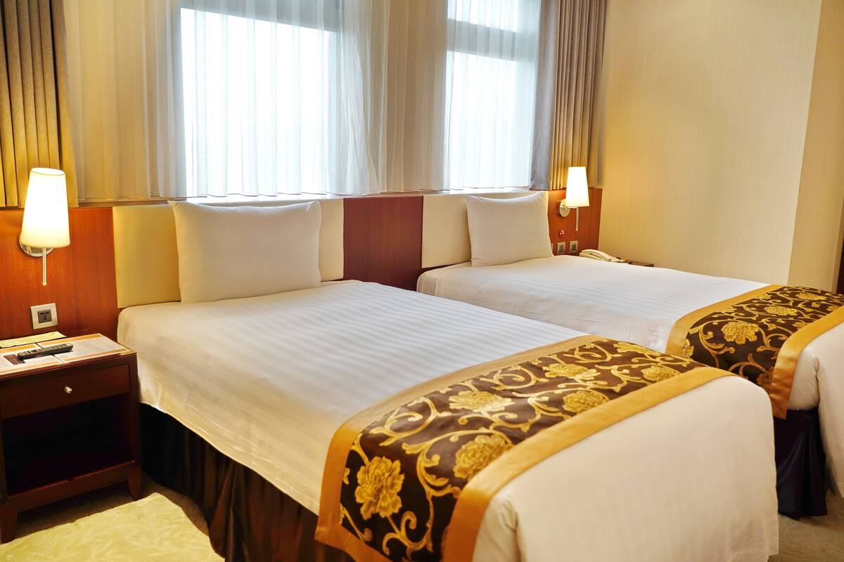 A hotel room with two beds, a nightstand, a lamp, and a telephone.