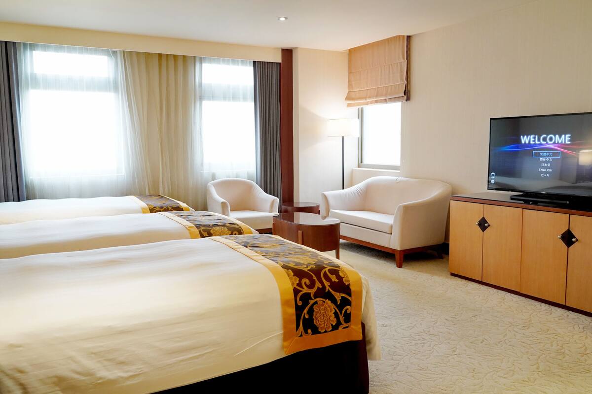 A hotel room with two beds, a television, a sofa, and a cabinet.
