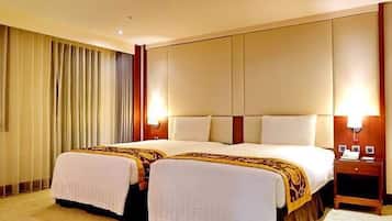 A hotel room with two beds, a large window with curtains, a bedside table with a lamp, and a nightstand with a phone and a book.