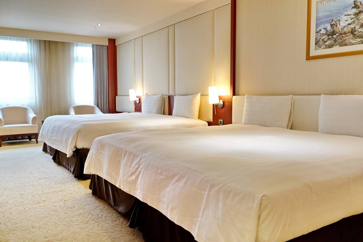 A hotel room with two large beds, a sofa, and a painting on the wall.