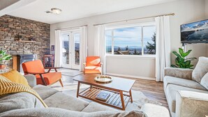 Una sala de estar con pared de piedra, chimenea, ventana grande con vistas y televisor de pantalla plana.