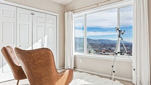 Habitación con un amplio ventanal que ofrece vistas a la ciudad, un trípode con un telescopio y dos sillones de cuero marrón.