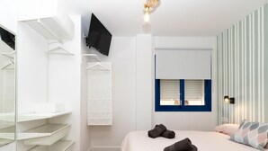 A bedroom with a bed, a TV mounted on the wall, a window with blinds, and a striped wall.