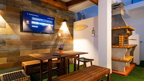 A wooden table and bench set in a room with a TV mounted on a wooden wall, a small shelf with items, and a wall with a map.