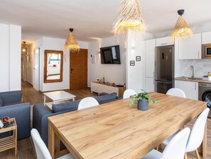 Une cuisine moderne avec des meubles blancs, un réfrigérateur en acier inoxydable et une table à manger en bois, assortie de chaises blanches.