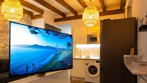 Una cocina moderna con lavadora incorporada, refrigerador y televisor de pantalla plana mostrando un paisaje.