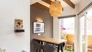 Cocina moderna con una mesa de madera, taburetes de bar, lámpara colgante y una estantería con vasos de cerveza.