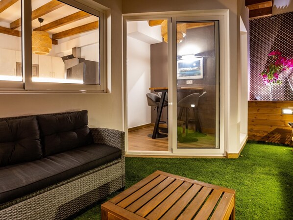Een gezellige zithoek met een donkerbruine bank, een houten salontafel en een glazen deur naar een eethoek met een tafel en stoelen.